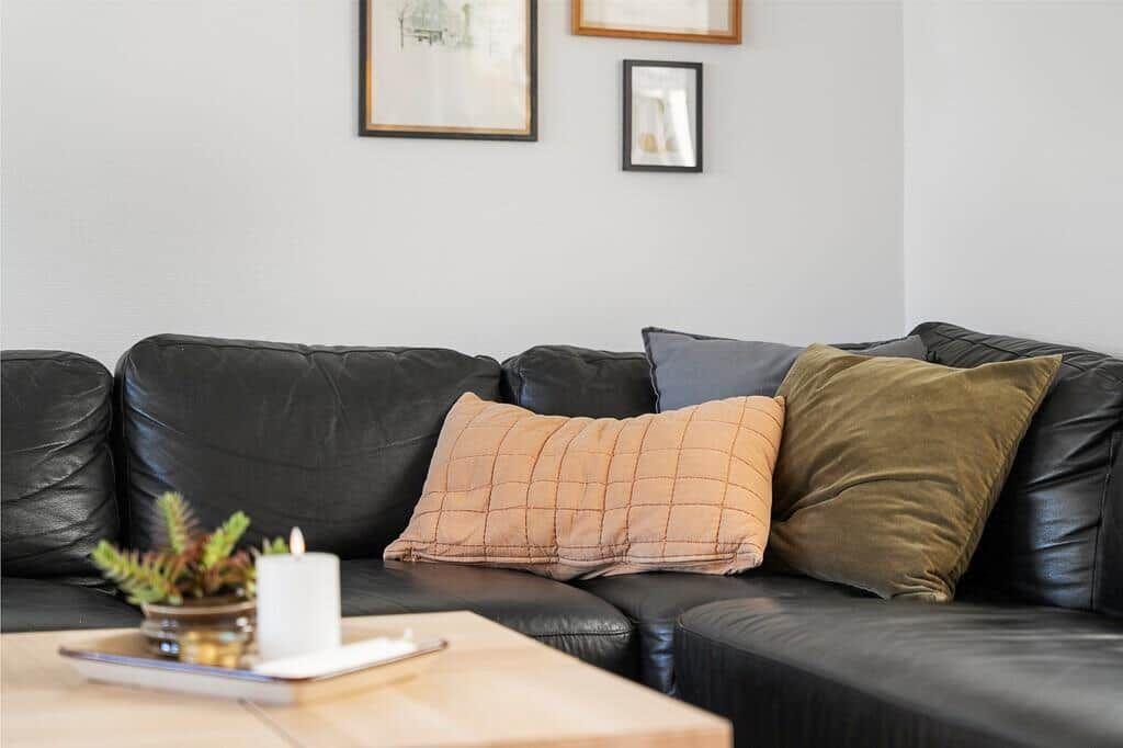 Schwarzes Ledersofa mit Kissen und Tisch vor Wand mit Bildern.
