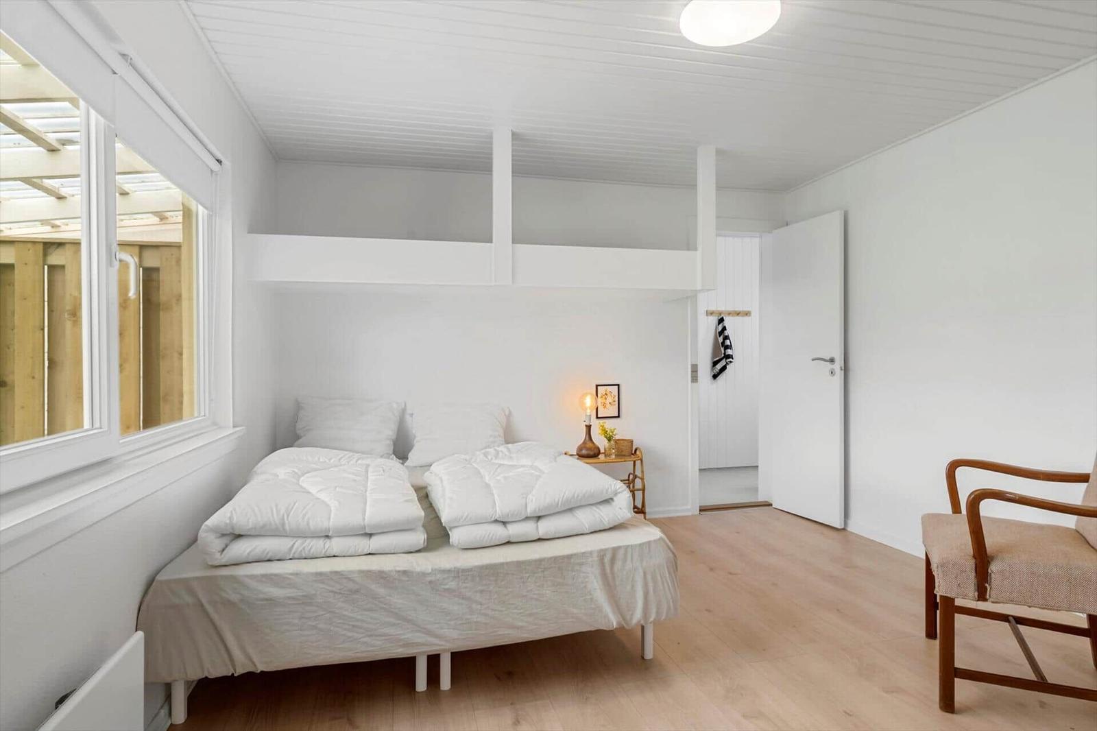 Schlafzimmer mit Doppelbett, Holzboden und großem Fenster. Helle Wände und Decke.