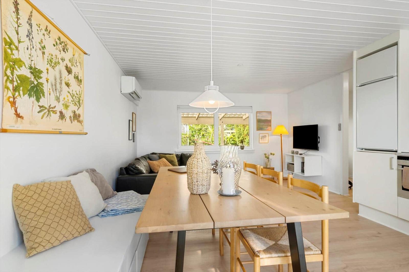 Essbereich mit Holztisch, Sofa und Küchenzeile. Wandbild und Fenster mit Blick auf Garten.