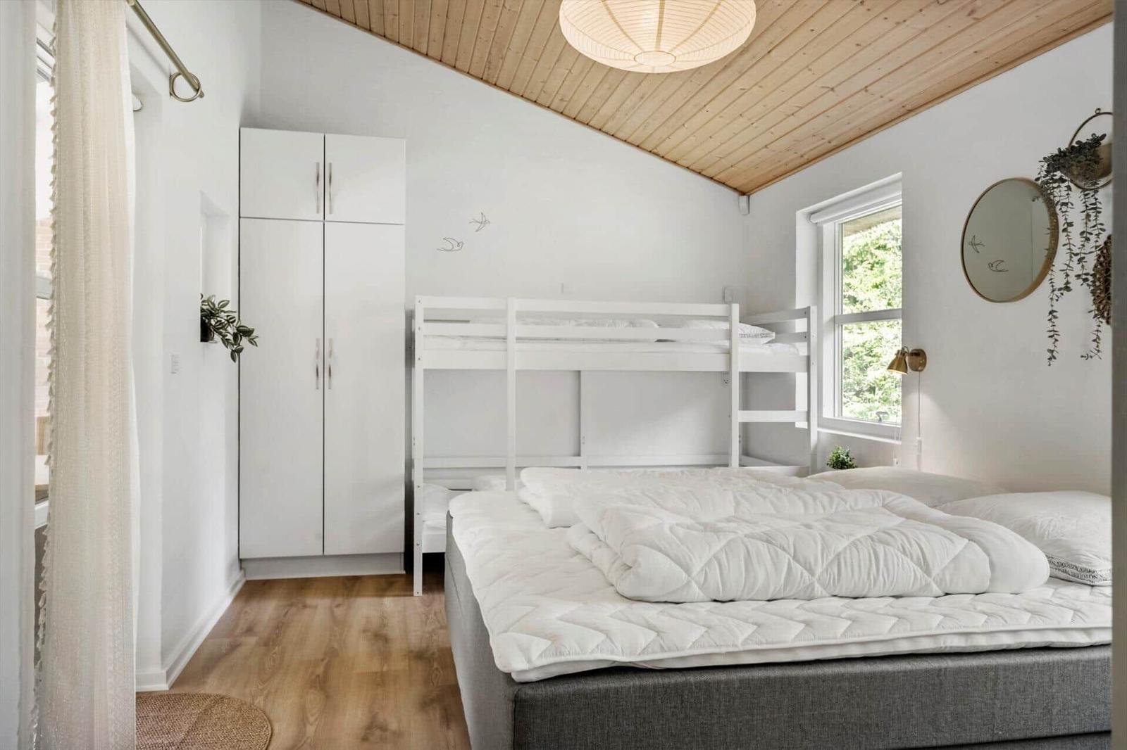 Schlafzimmer mit Doppelbett, Hochbett und Kleiderschrank. Holzdecke und Fenster mit Blick nach draußen.