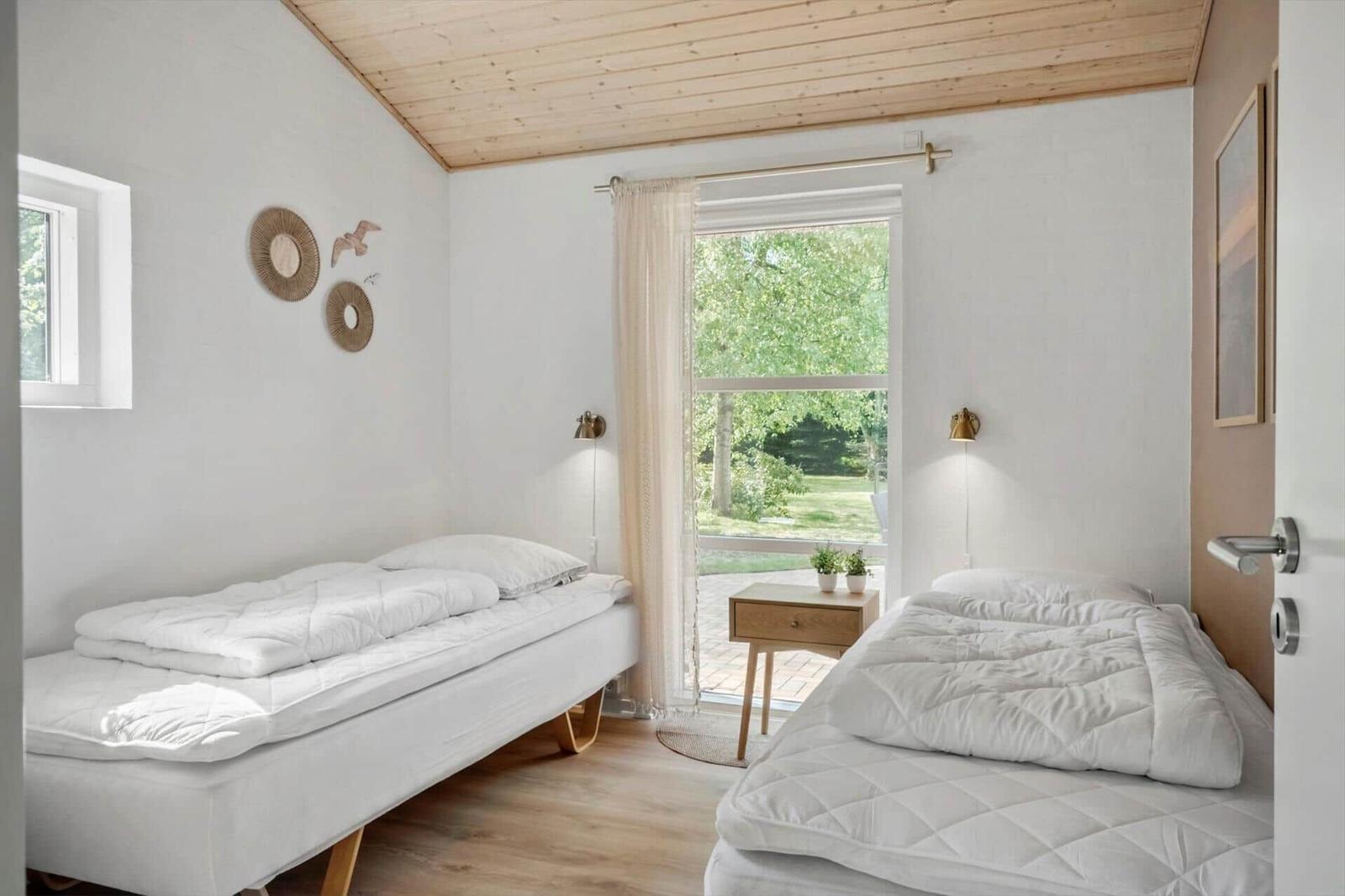 Zwei Betten mit weißen Bettwäsche, Holzdecke und Fenster mit Blick auf Grün.