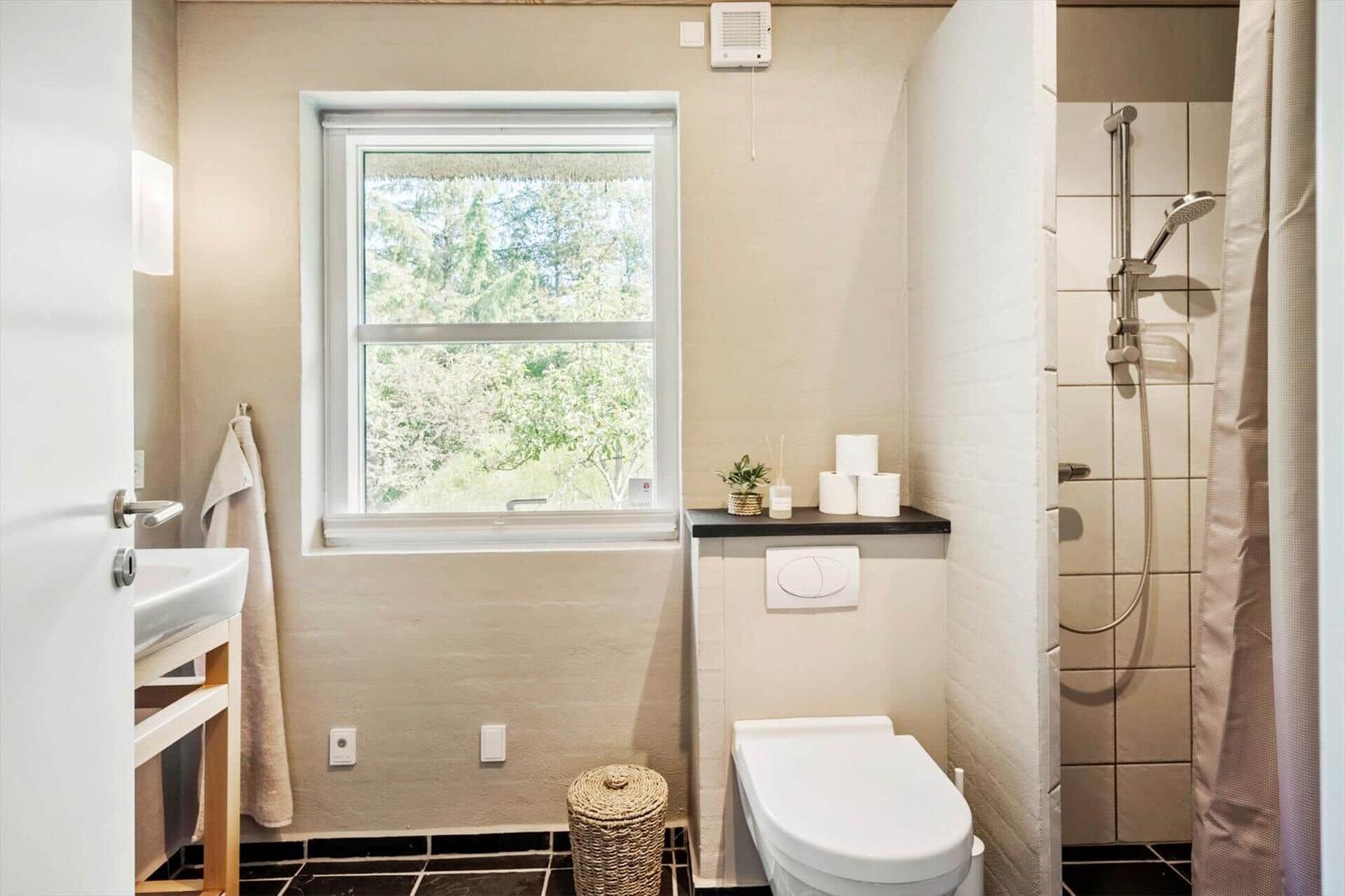 Badezimmer mit Toilette, Dusche und Fenster mit Blick auf Bäume.