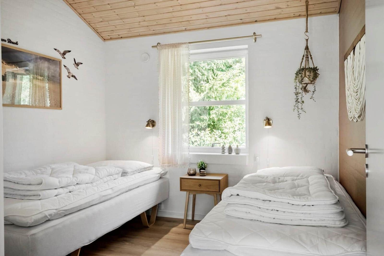 Zwei Betten mit weißen Bettwäschen, Fenster mit Vorhang und Holzdecke.