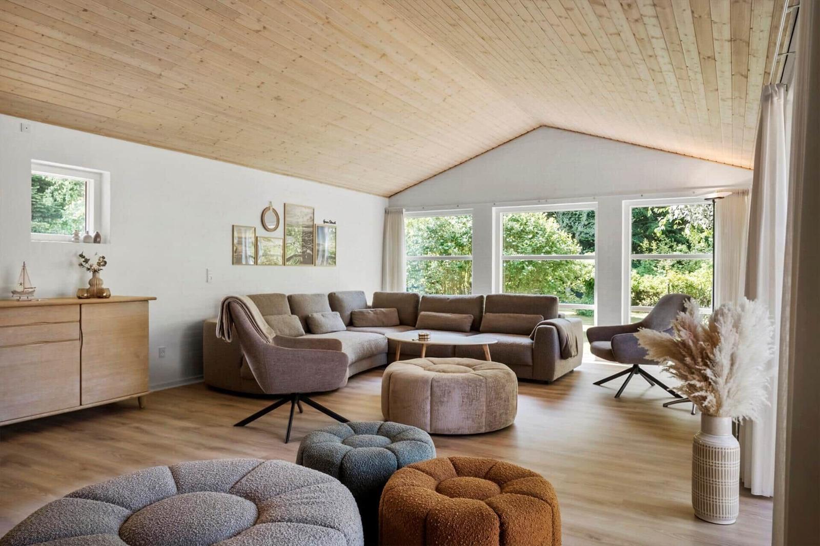 Wohnzimmer mit Holzdecke, Sofa, Sessel und Fenstern zum Garten