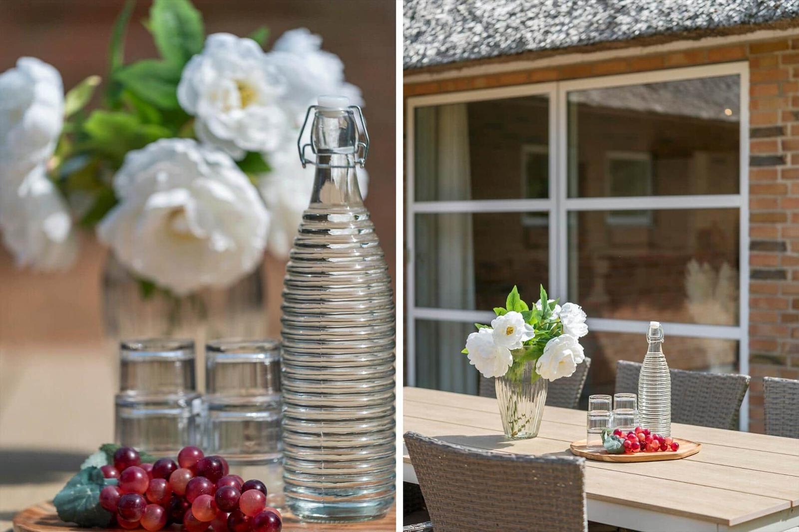 Terrasse mit Tisch, Stühlen, Blumen und Obst. Hintergrund: Haus mit Fenstern.