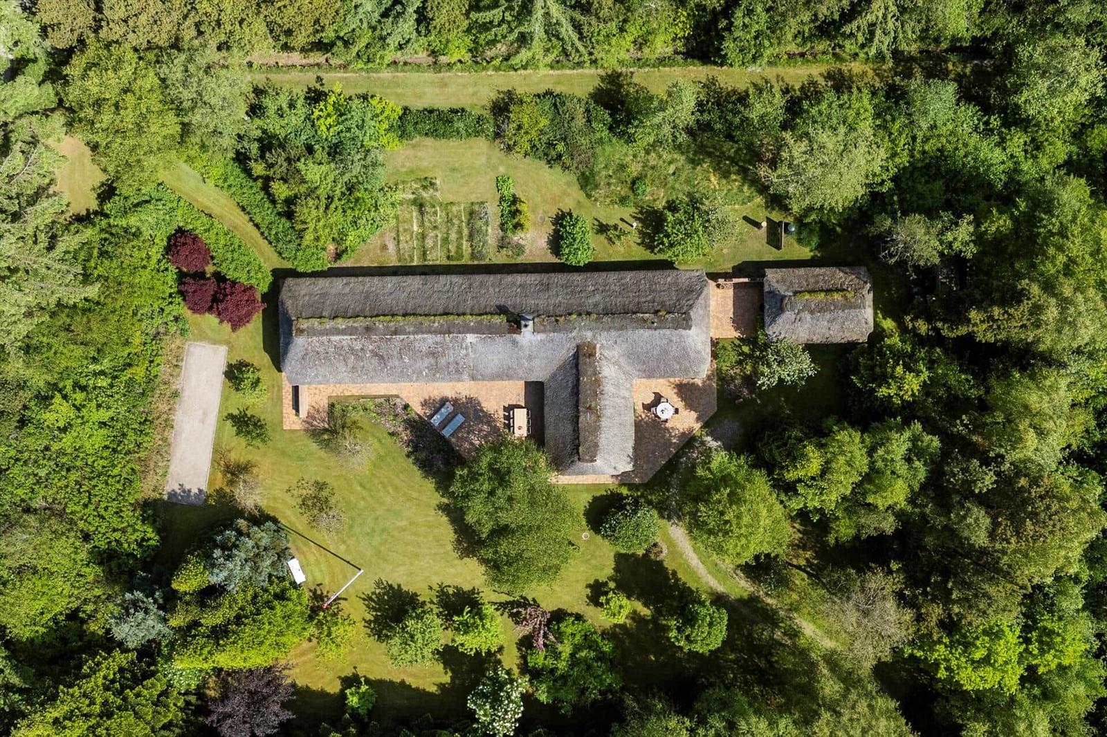 Haus mit Dach aus Stroh, umgeben von Wald und Garten.