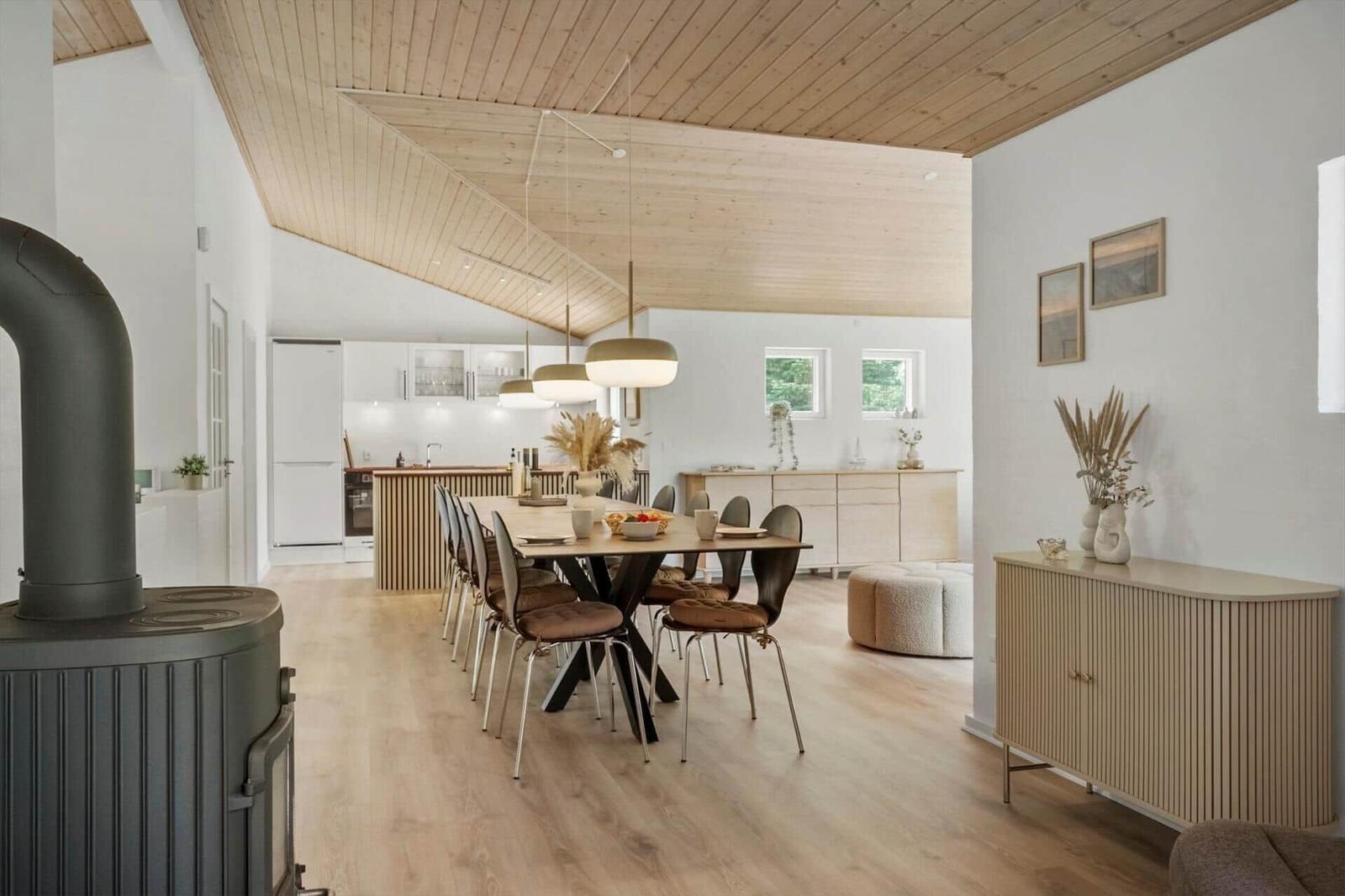 Haus mit Essbereich, Küche und Holzdecke. Esstisch mit Stühlen und Kamin.