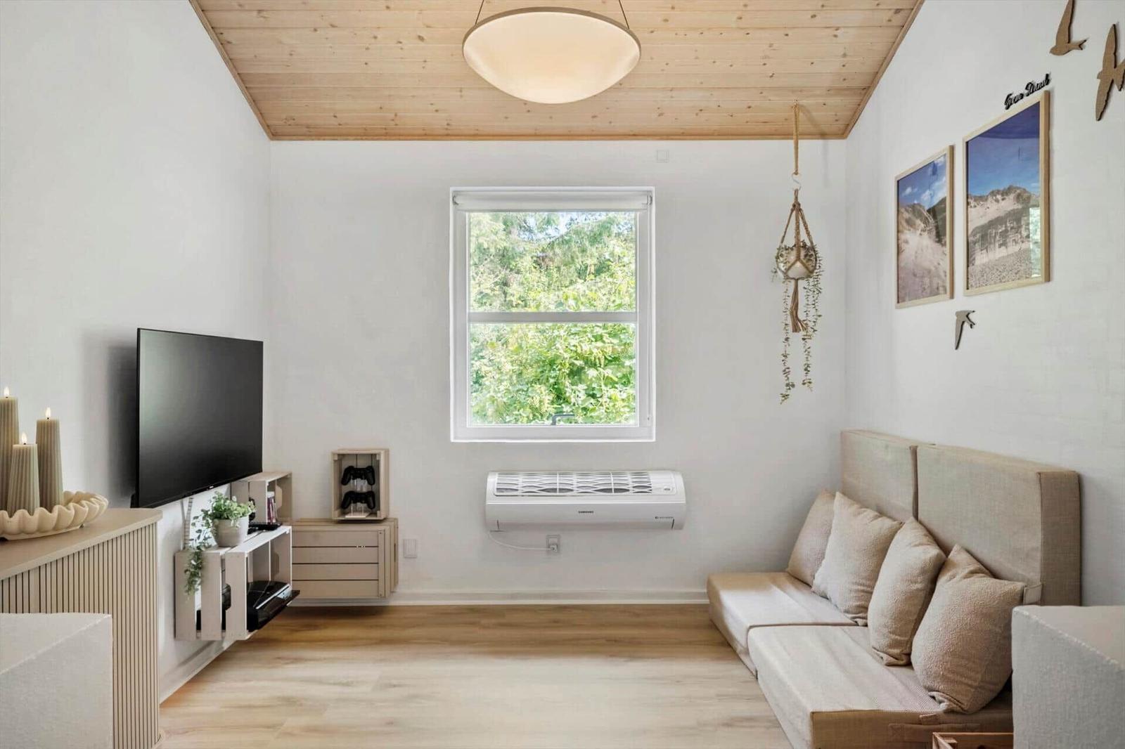 Wohnzimmer mit Sofa, Fernseher und Fenster mit Blick auf Bäume.