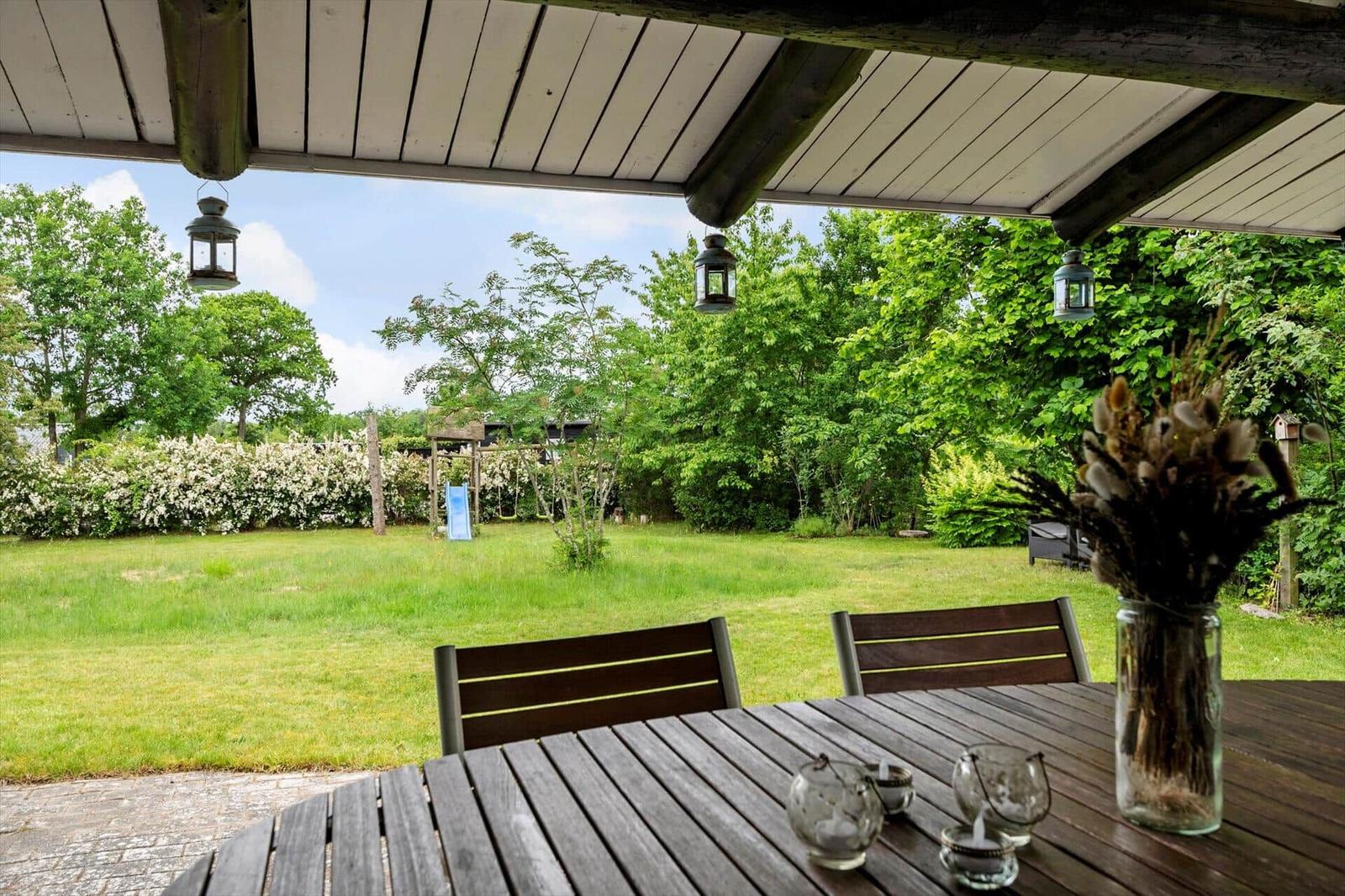 Patio with table and chairs, view of green garden with trees and playground.