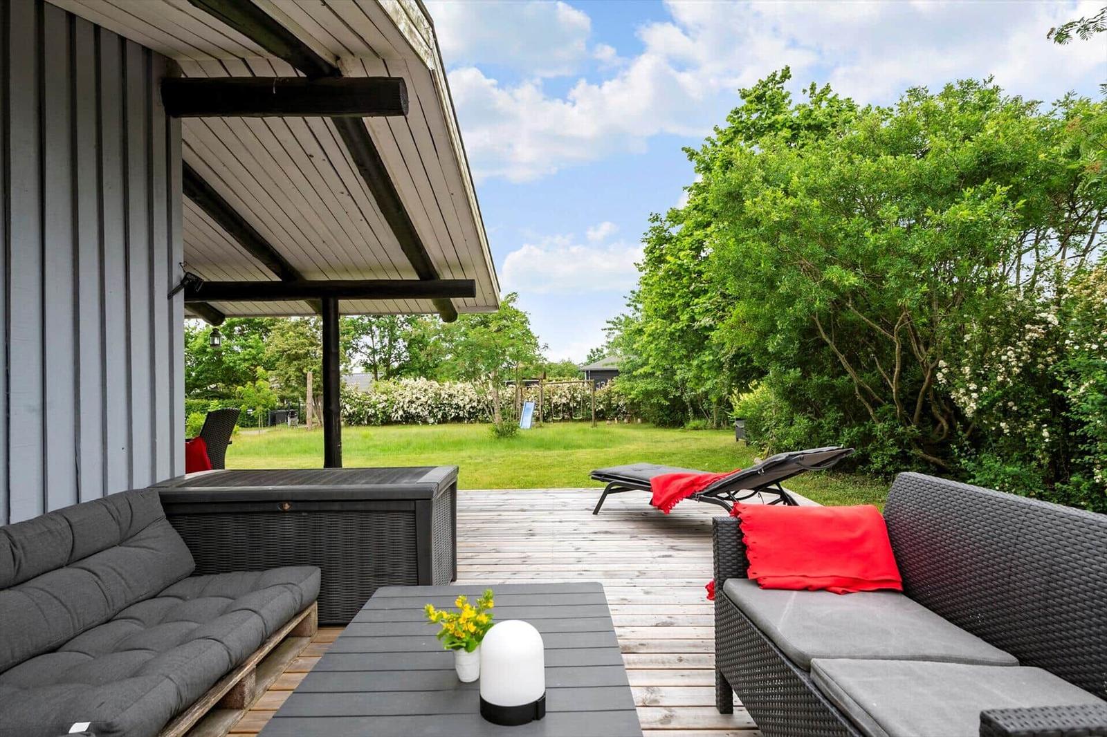 Terrace with seating, lounger, and garden view under blue sky.