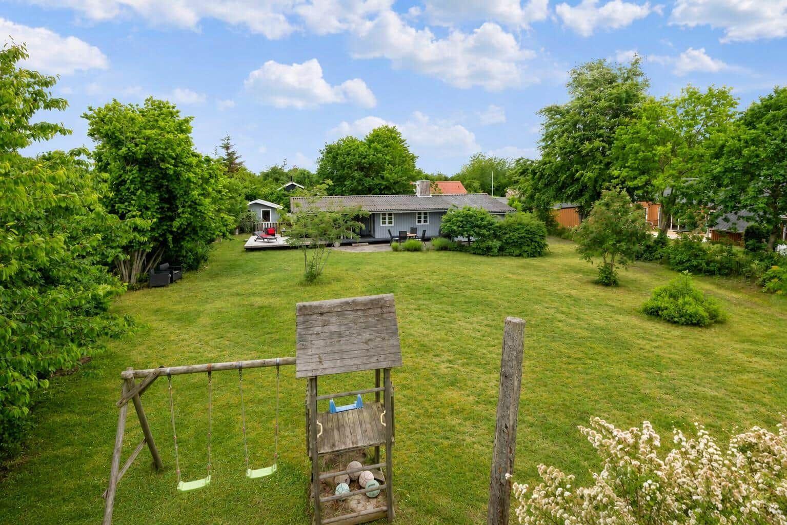 House with large garden, playground, and terrace under blue sky.