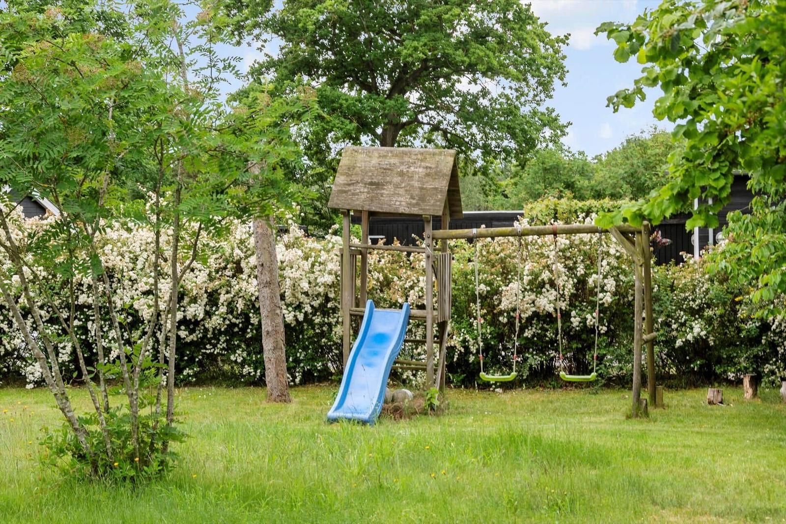 Backyard with playground, swing set, and slide. Surrounded by grass and shrubs.