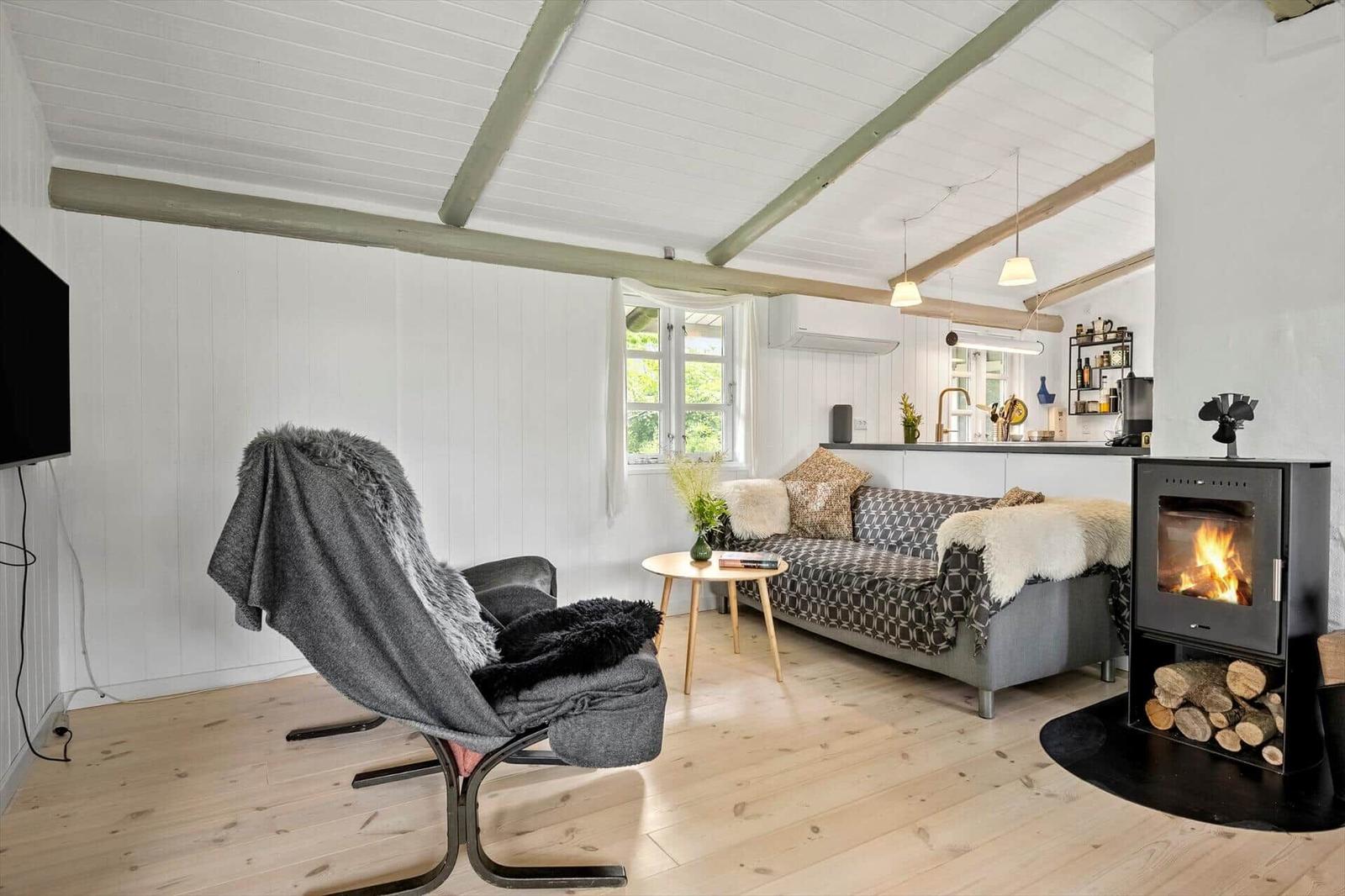 Living room with fireplace, sofa, and armchair. Wooden floor and white walls.