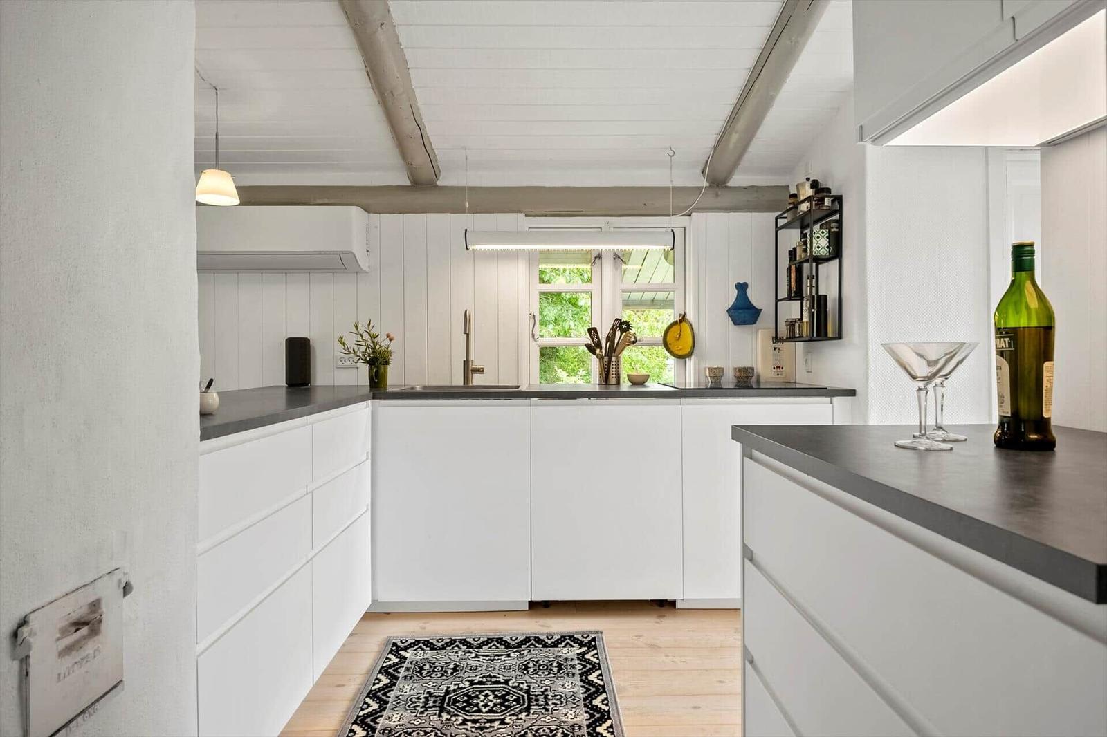 Kitchen with white cabinets, dark worktop, and wooden floor. Window with view of greenery.