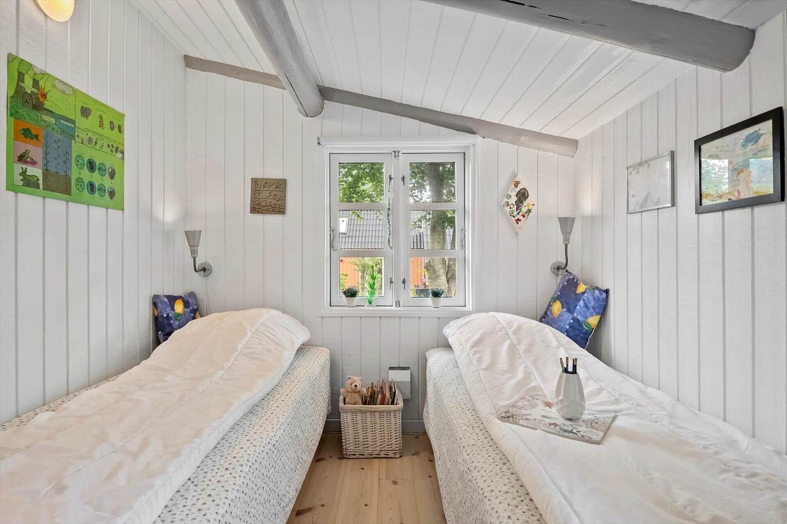 Two beds with white bedding are in a room with white paneled walls and a window.