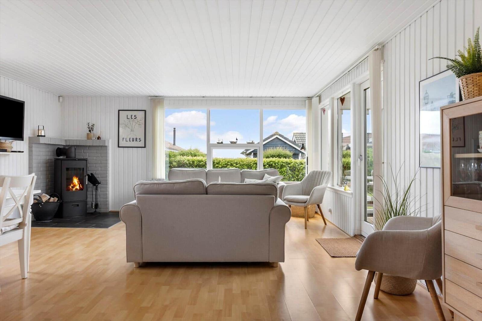 Wohnzimmer mit Sofa, Kamin und großen Fenstern. Holzboden und weiße Wände.