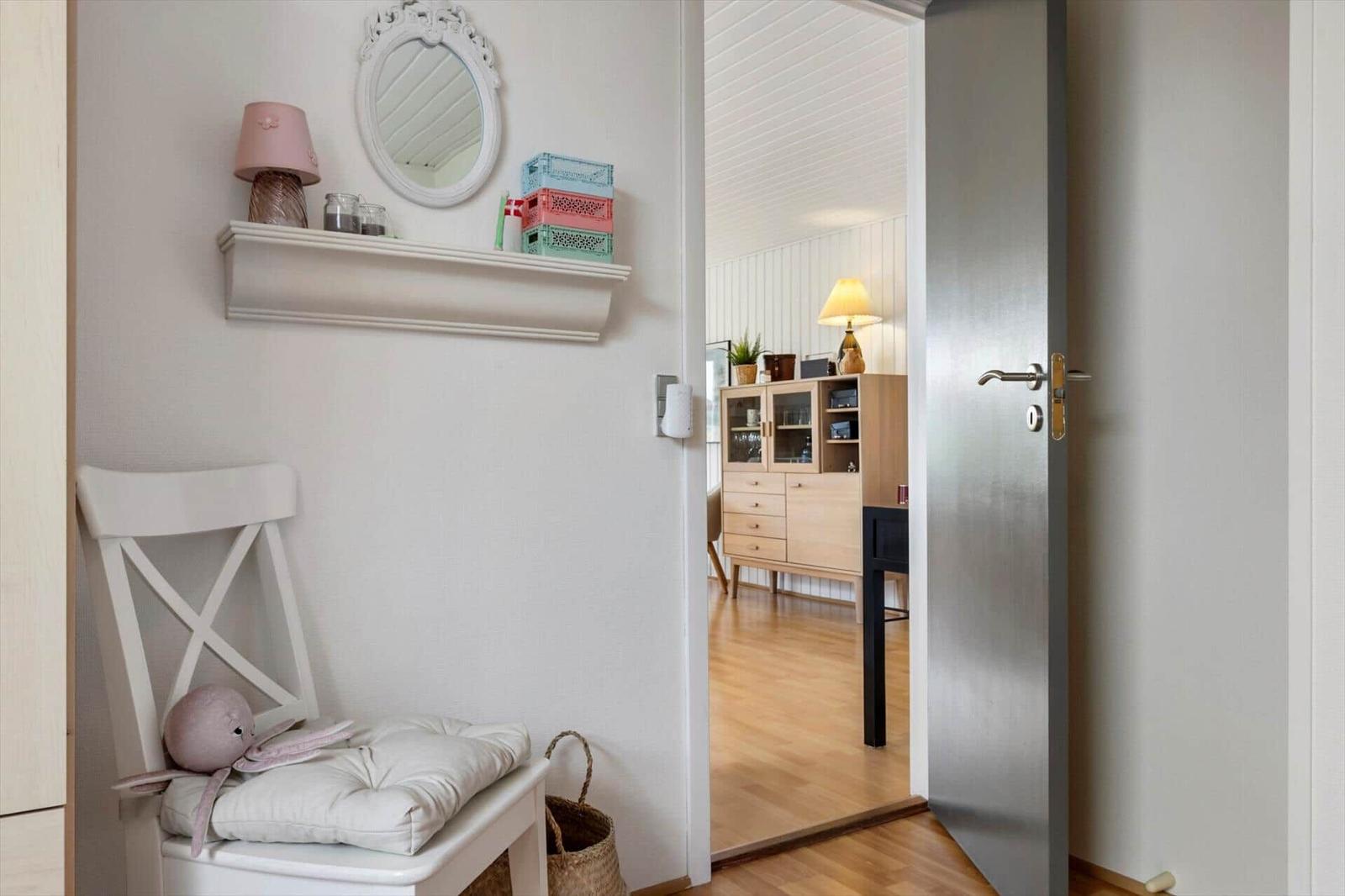 Ein Eingangsbereich mit Stuhl, Spiegel und Kiste. Durchgang zu einem Raum mit Schrank und Lampe.