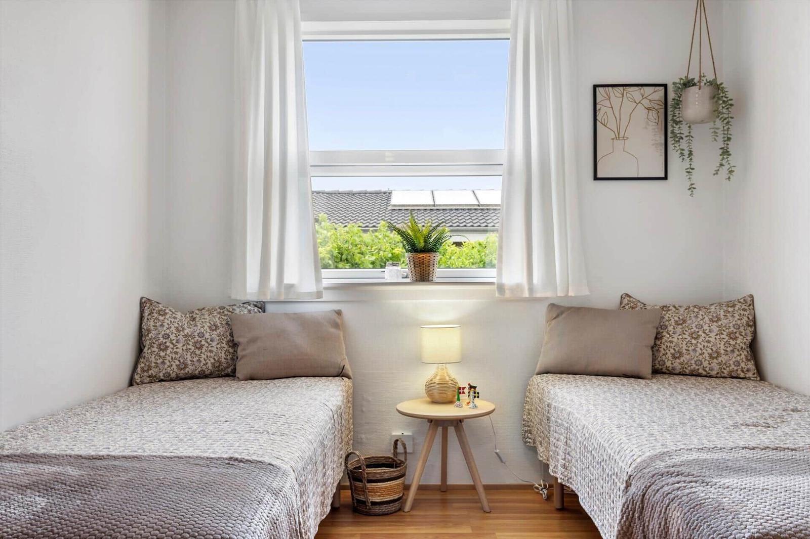 Zwei Betten mit Kissen und Decke stehen unter einem Fenster mit Blick auf Dächer und Grün.