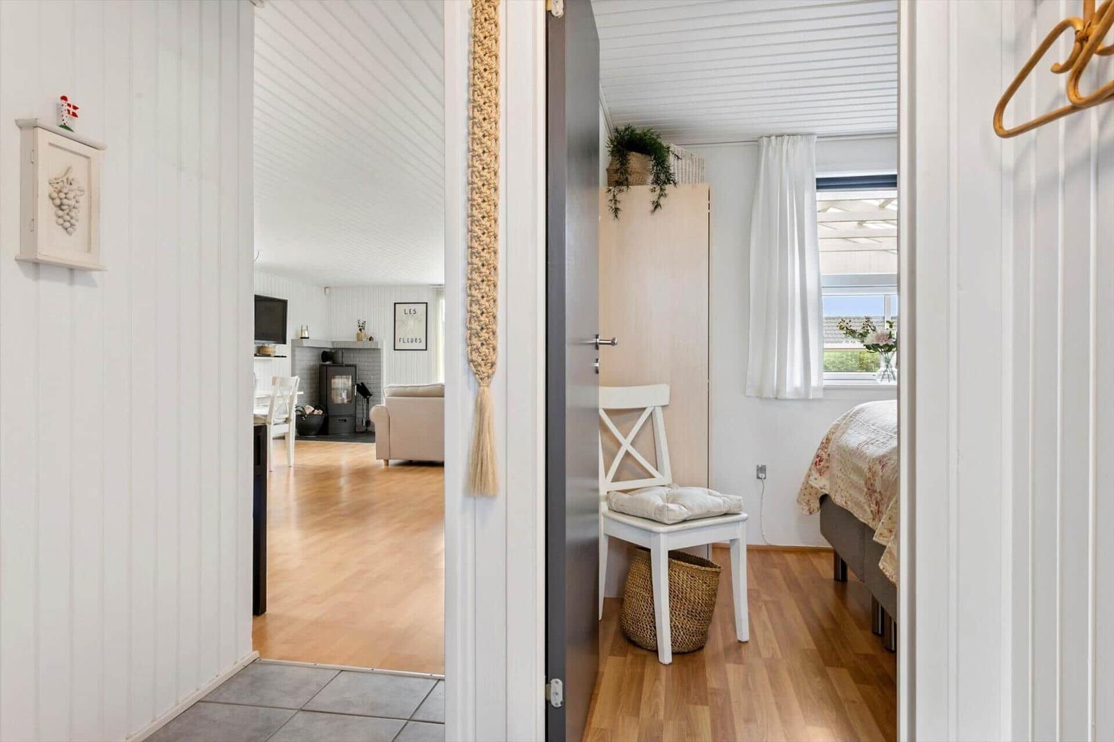 Schlafzimmer mit Bett, Stuhl und Fenster. Blick in Wohnzimmer mit Kamin und Holzboden.