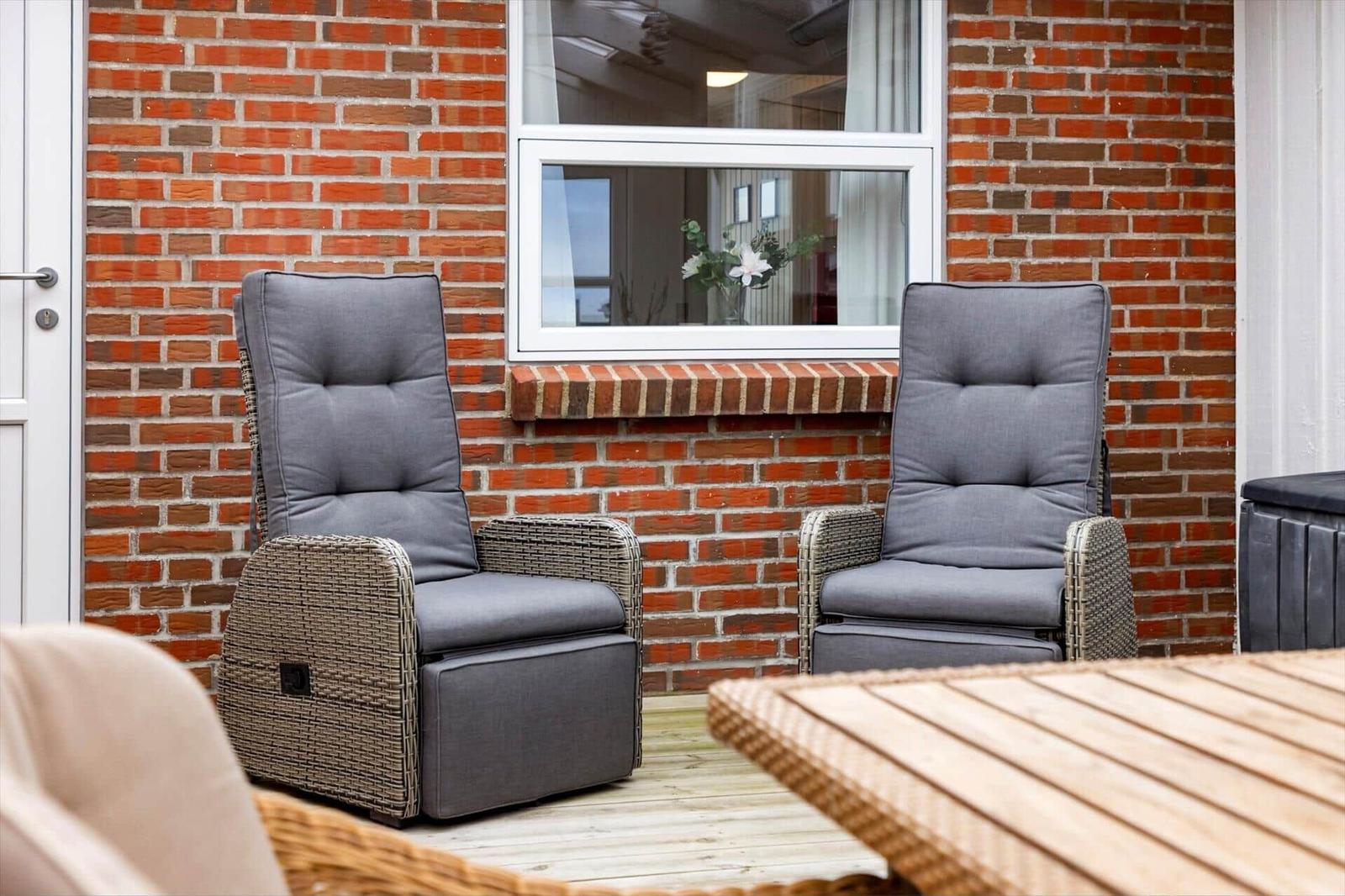 Zwei graue Sessel mit Rückenlehnen stehen auf einer Terrasse vor einer Backsteinwand.