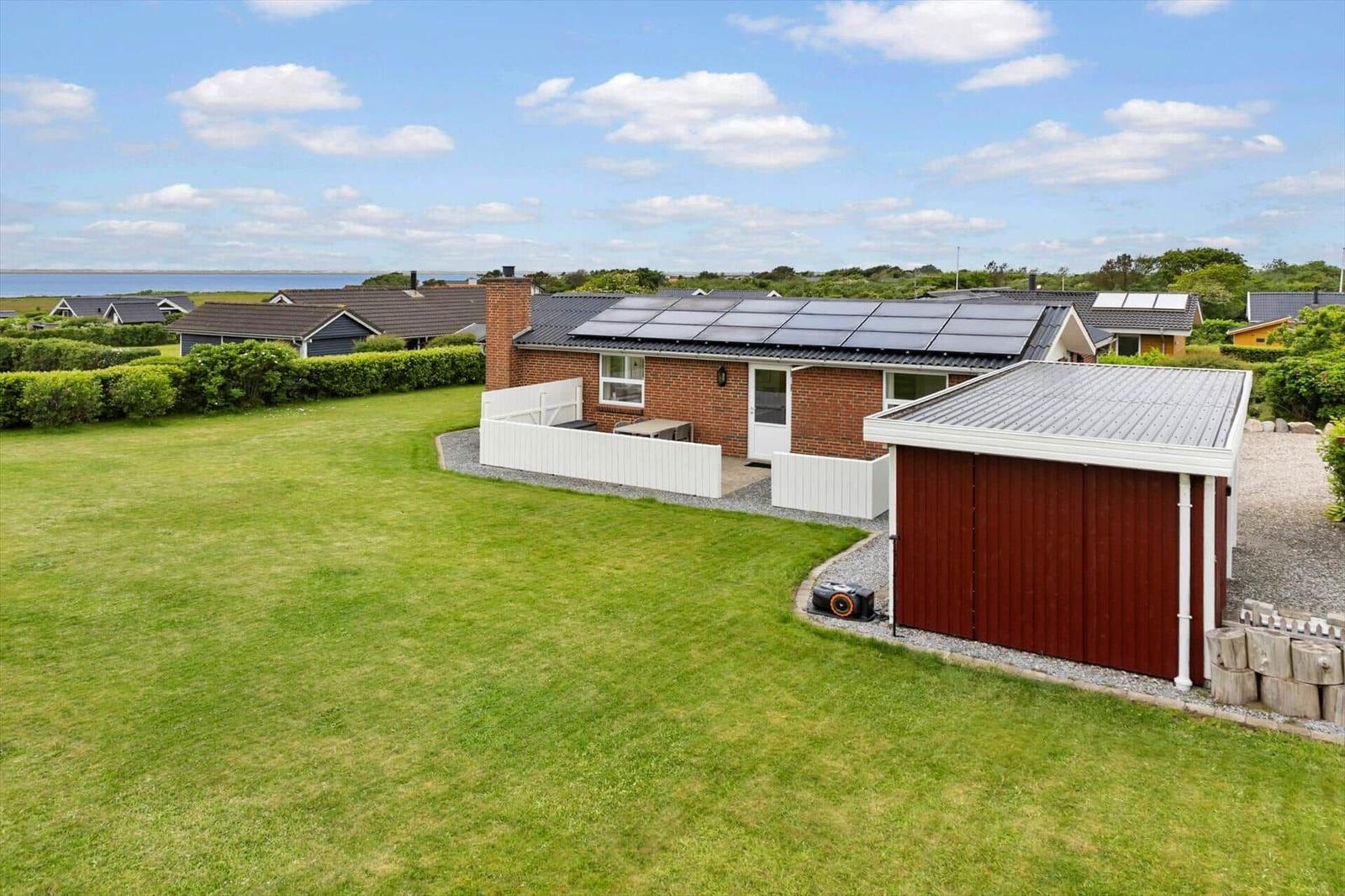 Einfamilienhaus mit Solaranlage, großem Garten und Garage. Blick auf Wasser im Hintergrund.