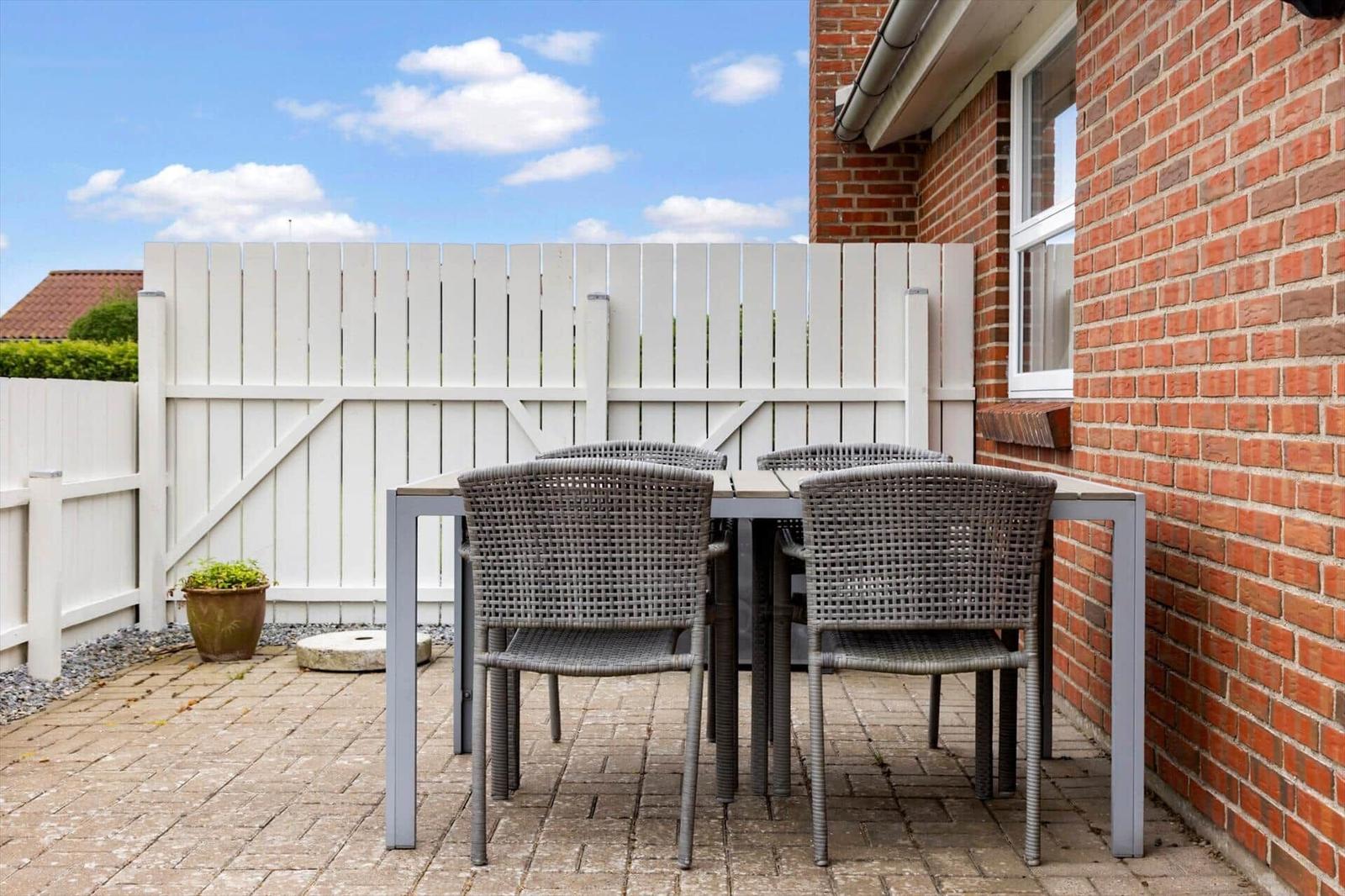 Terrasse mit Tisch und Stühlen neben rotem Backsteinhaus mit weißem Zaun.