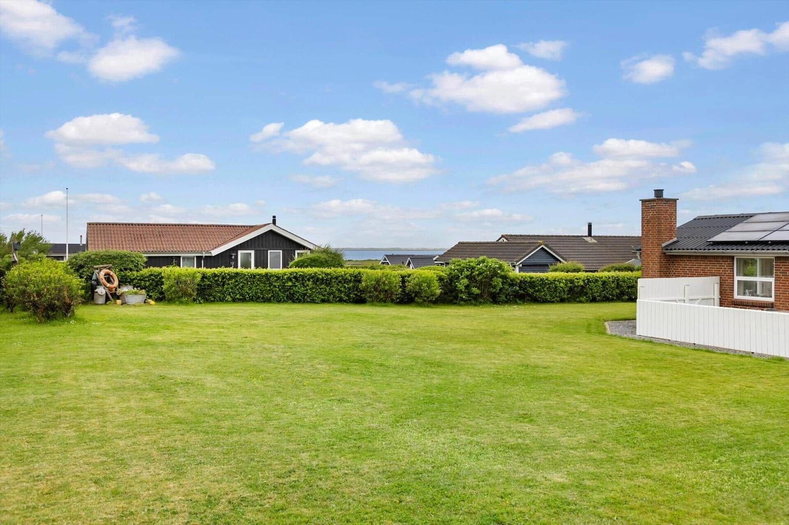 Großer grüner Garten mit Hecke und Häusern im Hintergrund unter blauem Himmel.