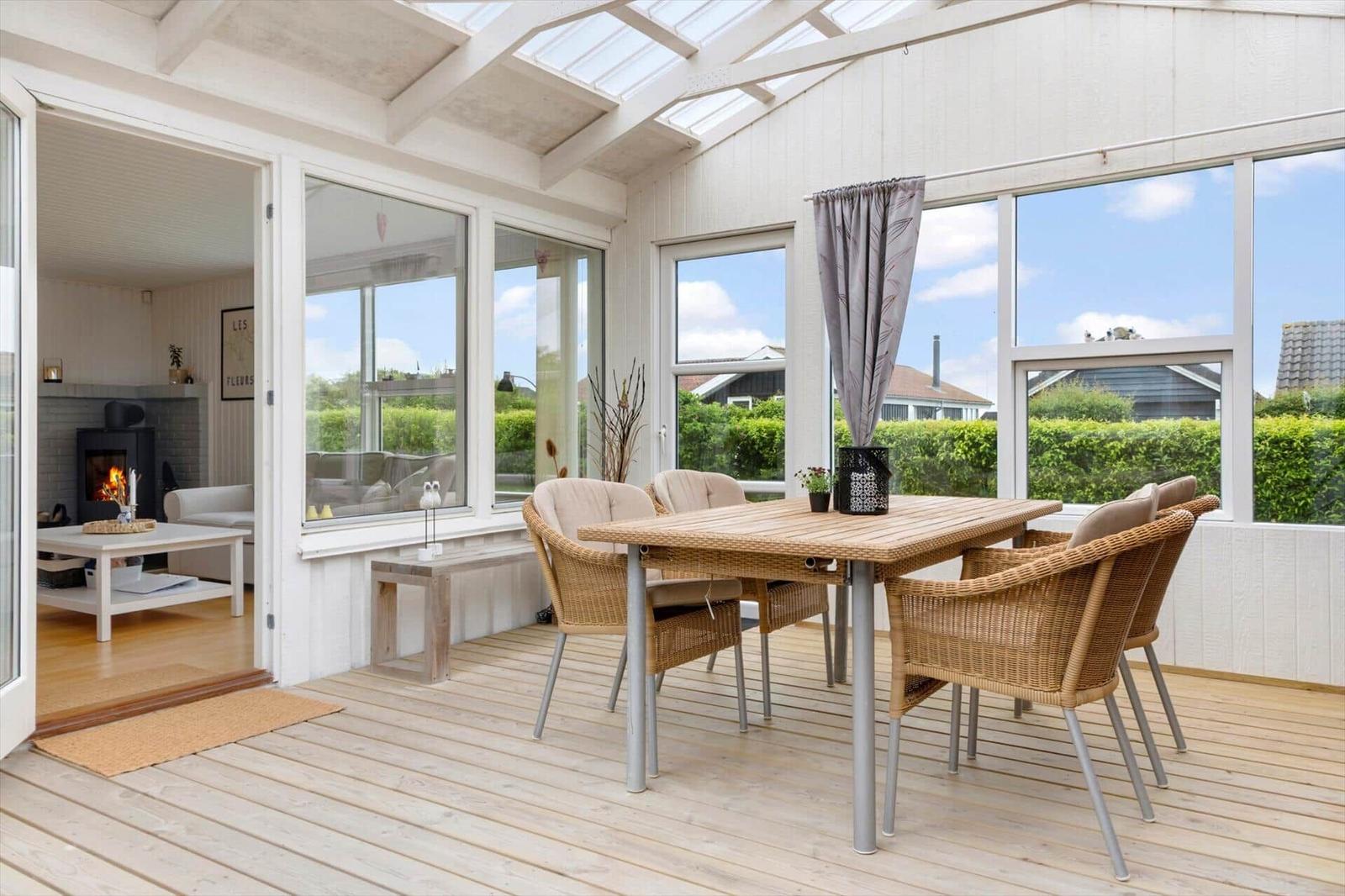 Terrasse mit Esstisch und Stühlen. Durchgehendes Glas ermöglicht Blick ins Wohnzimmer mit Kamin.