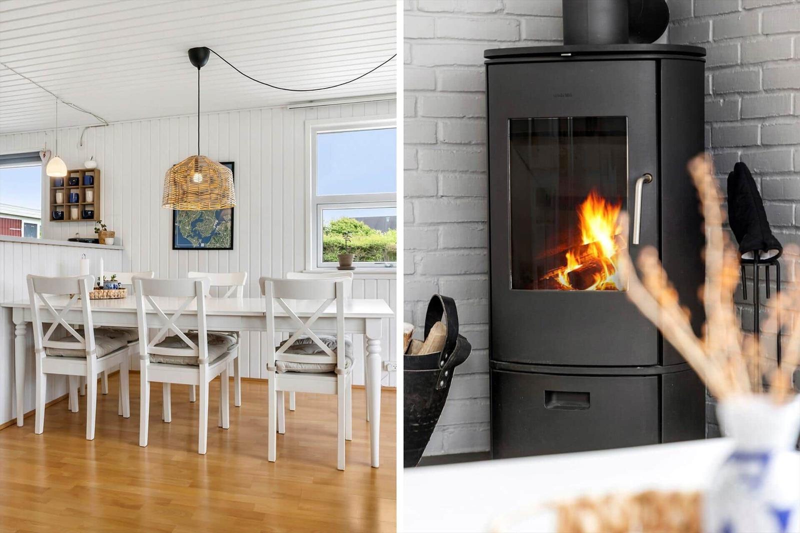 Esszimmer mit weißem Tisch und Stühlen, Holzboden und Fenster. Kaminofen mit brennendem Holz.