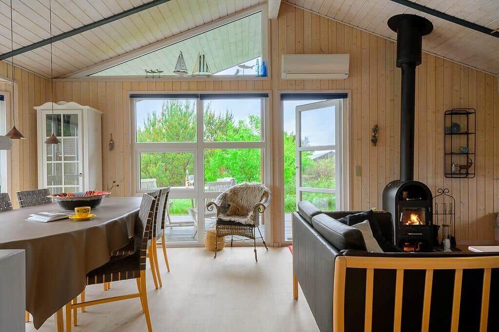 Living and dining area with wooden walls, wood stove, and large window to terrace.