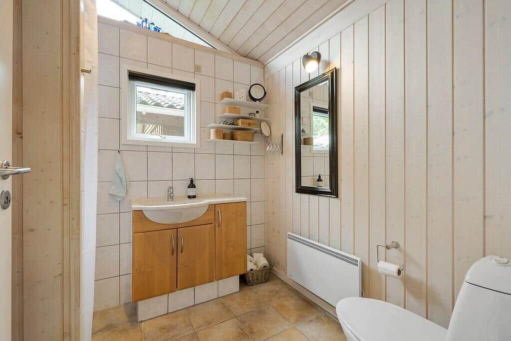 Bathroom with sink, mirror, and toilet. Wooden walls and tiled floor.