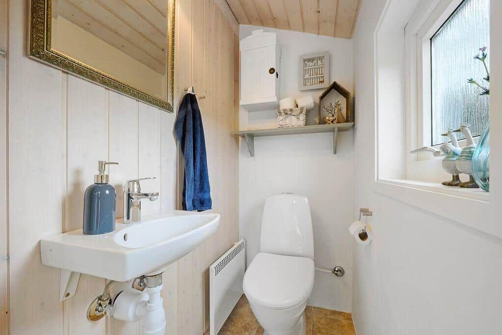 Bathroom with sink, toilet, and window. Wooden wall, mirror, and decorative items.