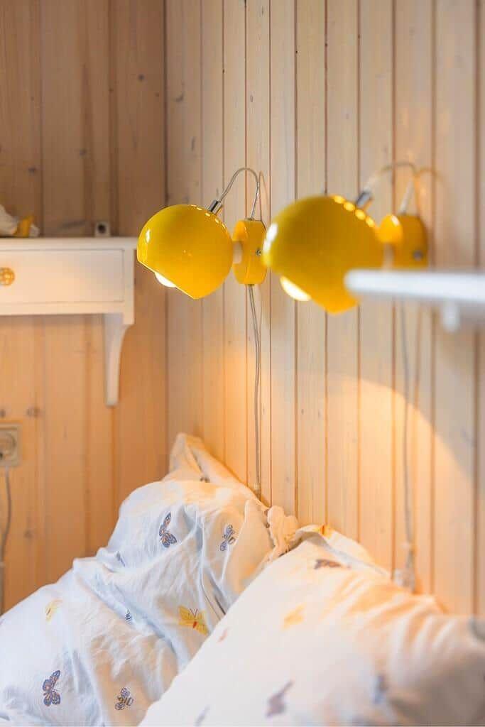 Bed head with yellow wall lamps and wooden wall in the bedroom.