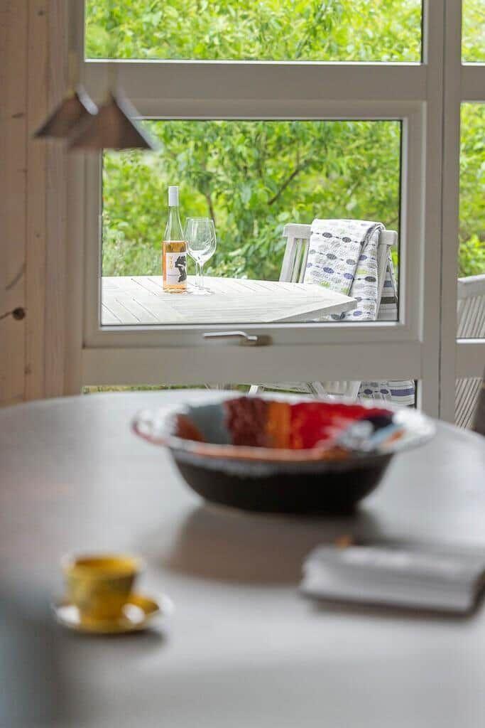 Table with cup and bowl in front of window with view of terrace and greenery.