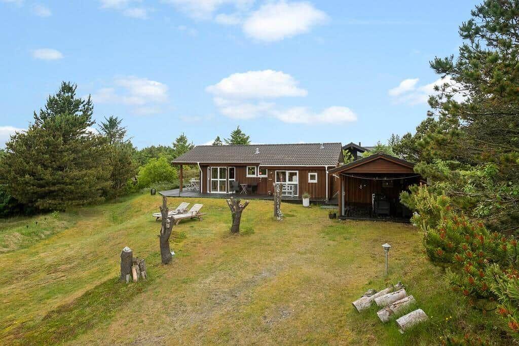 Wooden house with terrace, garden, and grill hut under blue sky.