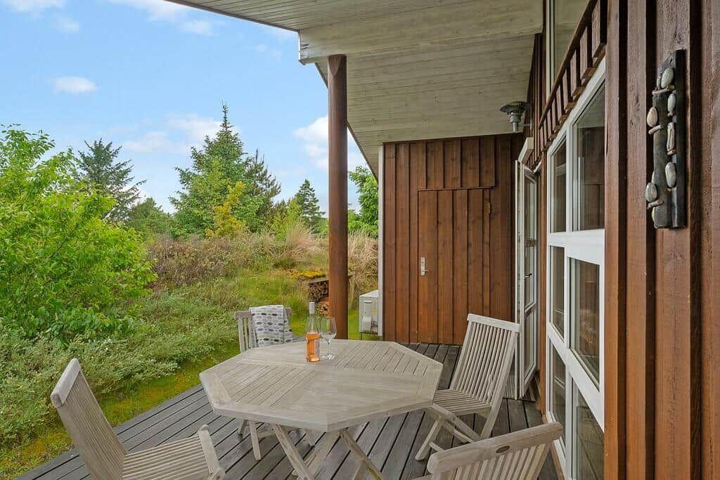 Deck with table and chairs, view of green landscape and wooden house.