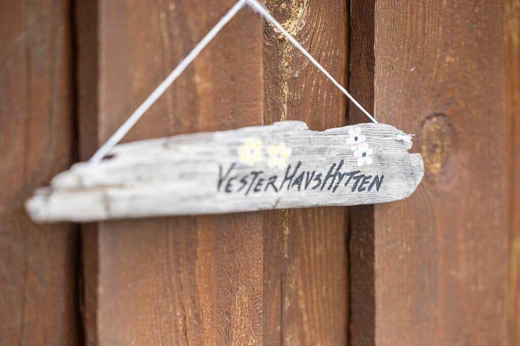 A wooden sign reading Vester Havshytten hangs on a wooden wall.