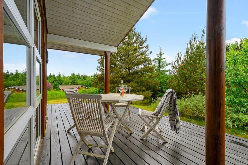 Deck with table and chairs, view of green trees and lawn.