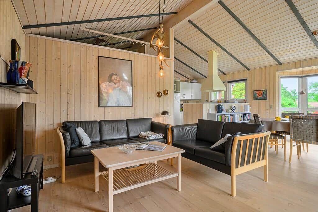 Living room with two black sofas, wooden table, and kitchen area in the background.