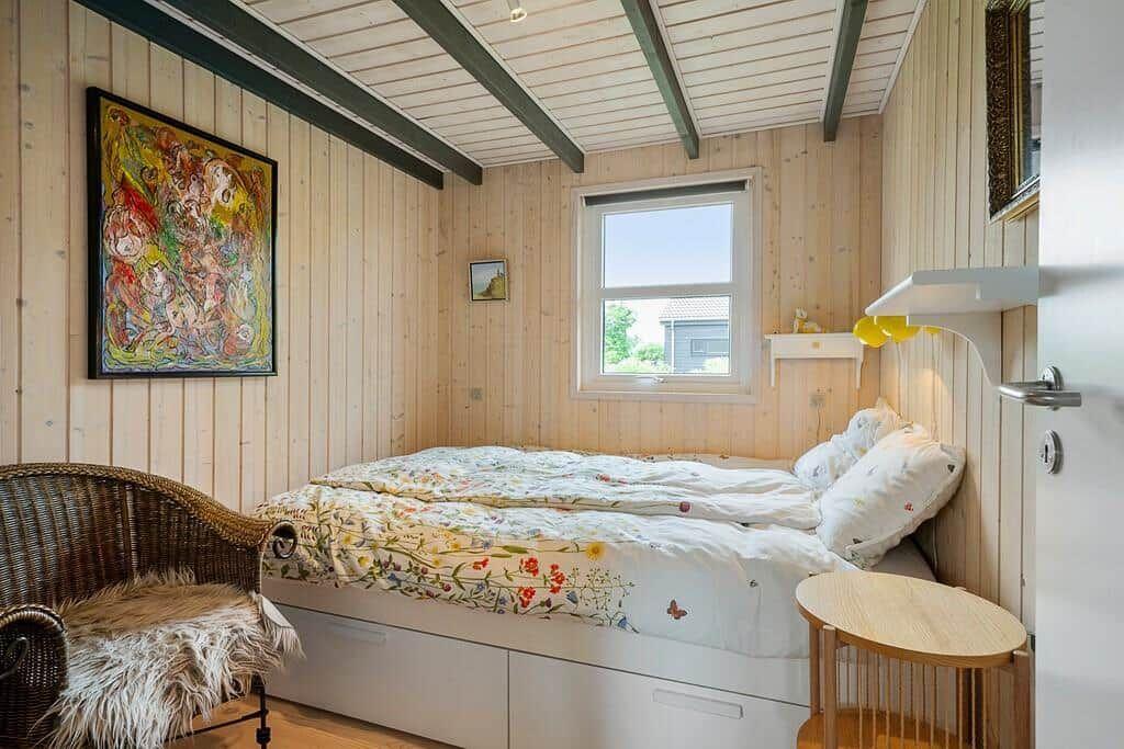 Bedroom with bed, wall art, window, and wicker chair.