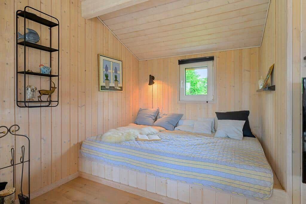 Bedroom with wooden walls, bed, and window. Shelf and wall picture visible.