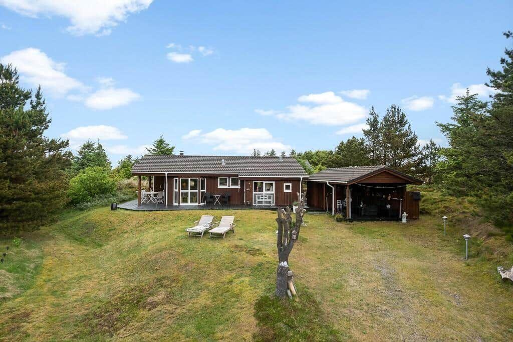 Wooden house with terrace, grill area, and lawn. Lounge chairs on grass.