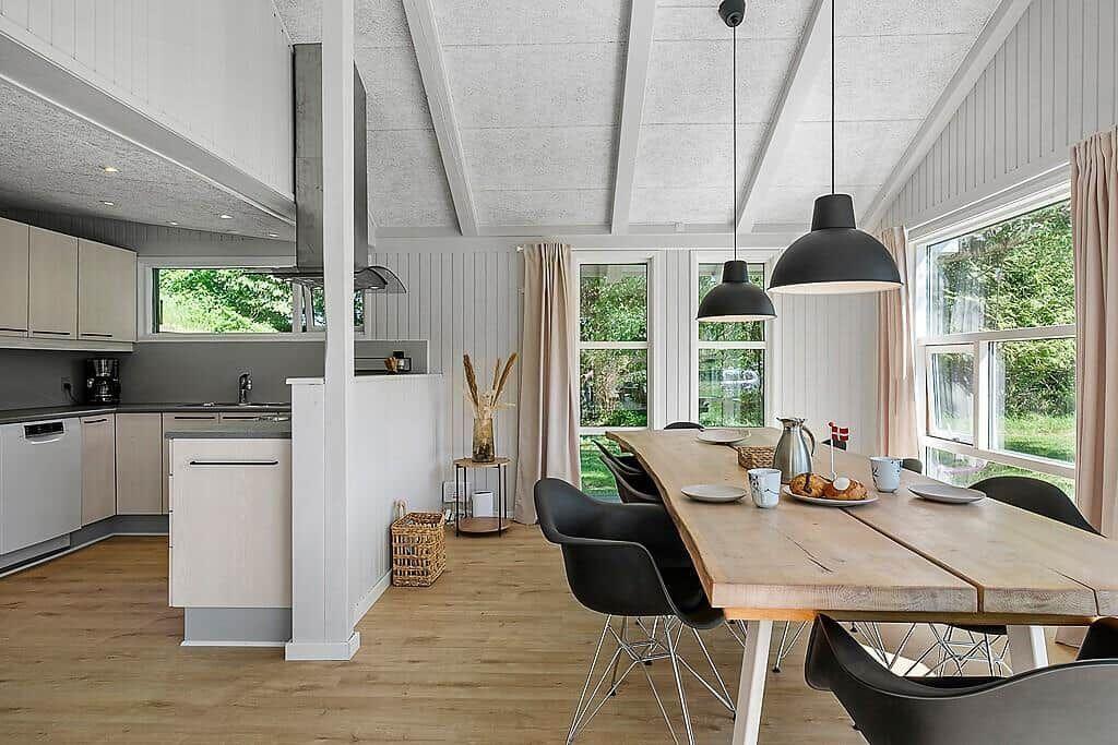 Kitchen and dining area with wooden table, black chairs, and large windows.