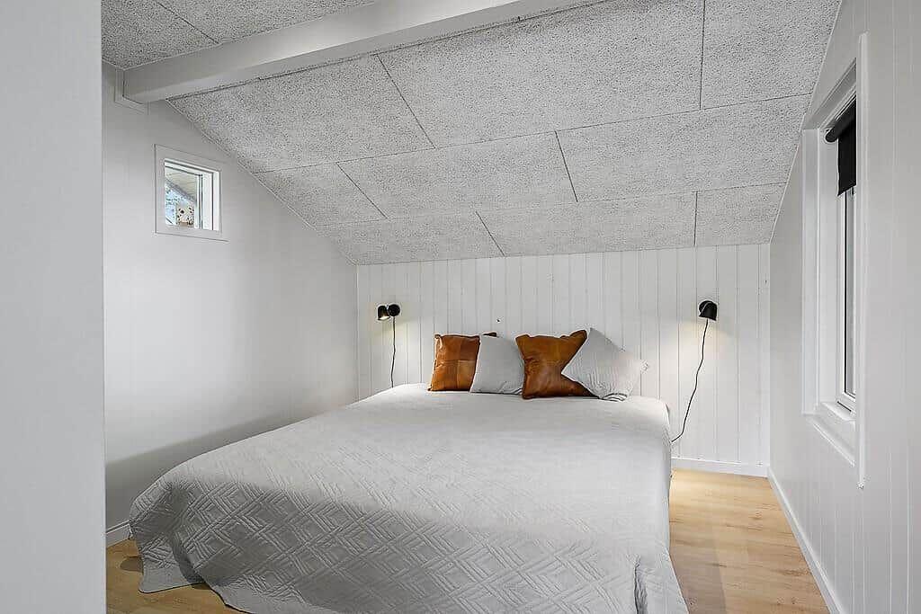 Bedroom with bed, two wall lamps, and wooden floor. Ceiling with panels and windows.