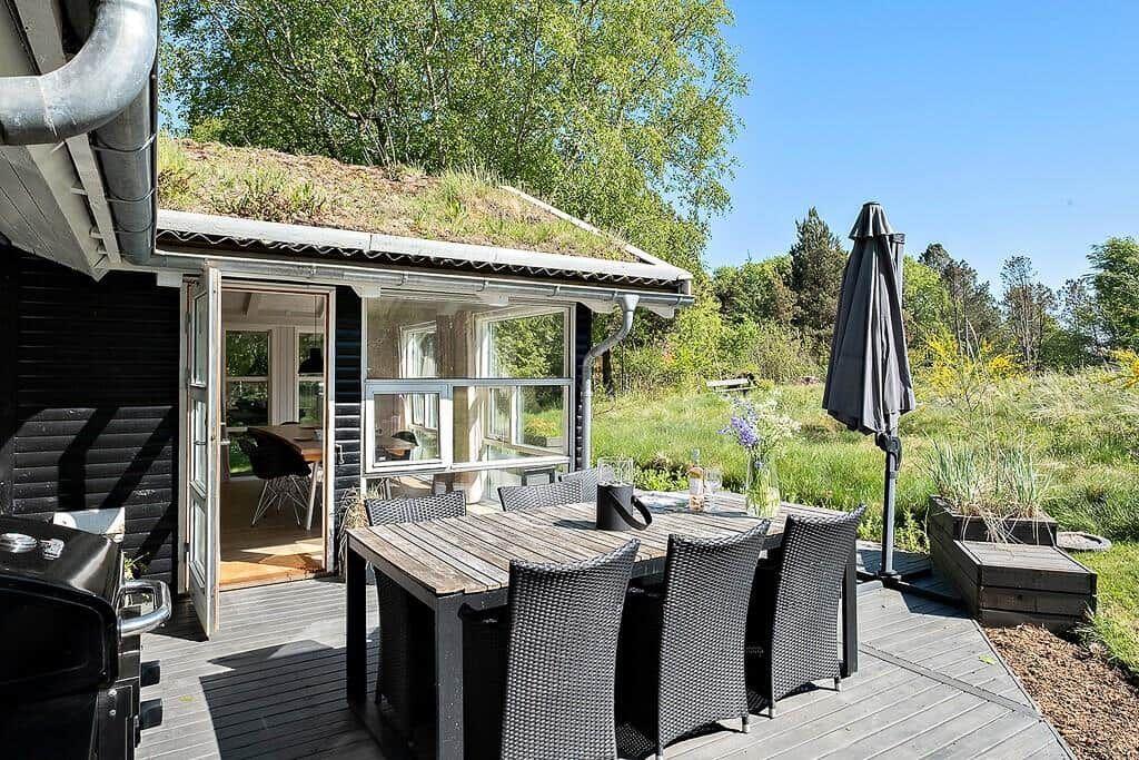 Deck with table, chairs, and umbrella. Background shows grassland and forest.