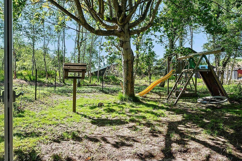 Backyard with playground, swing, and slide under trees.