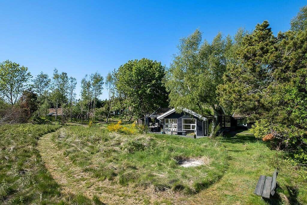 A small house with a terrace is situated among trees and grass.