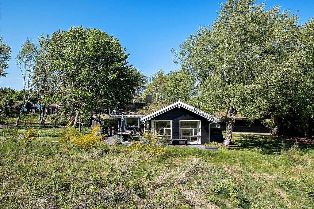 A small house with a terrace is surrounded by trees and grass.