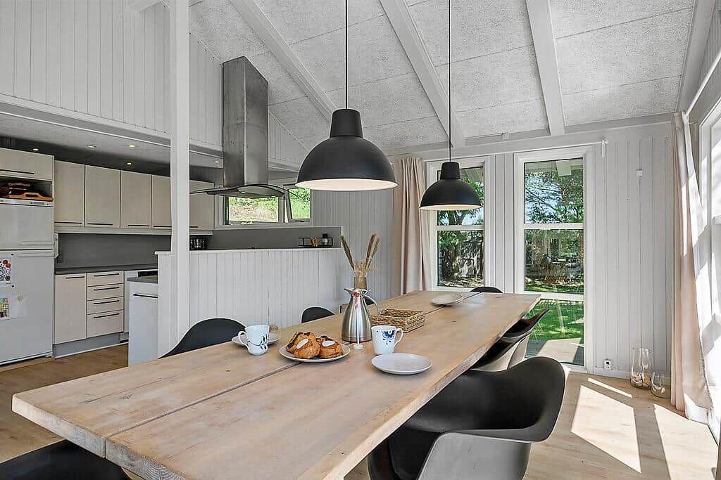 Dining area with wooden table, black chairs, and kitchen area in background.