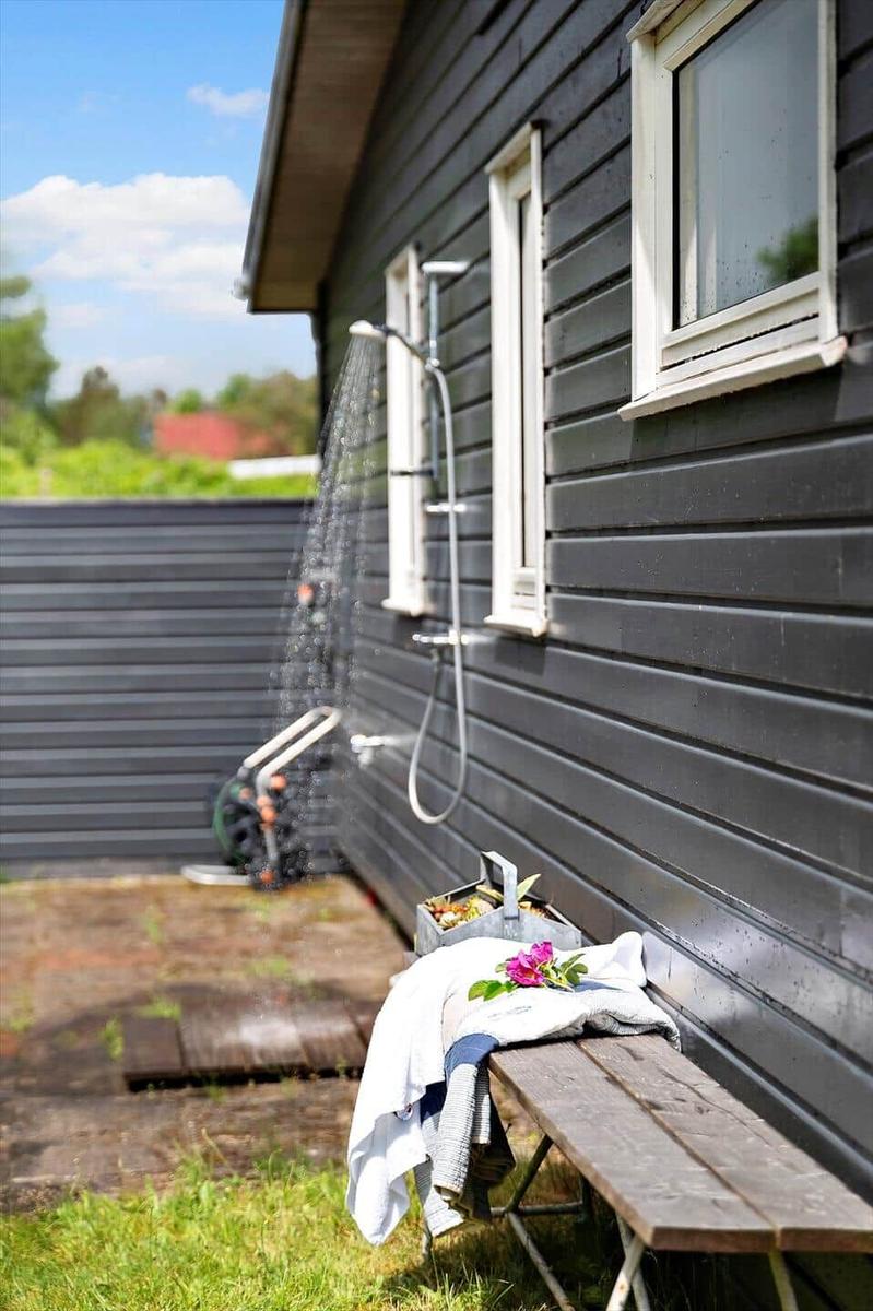 Outdoor shower on house wall with bench and towel.